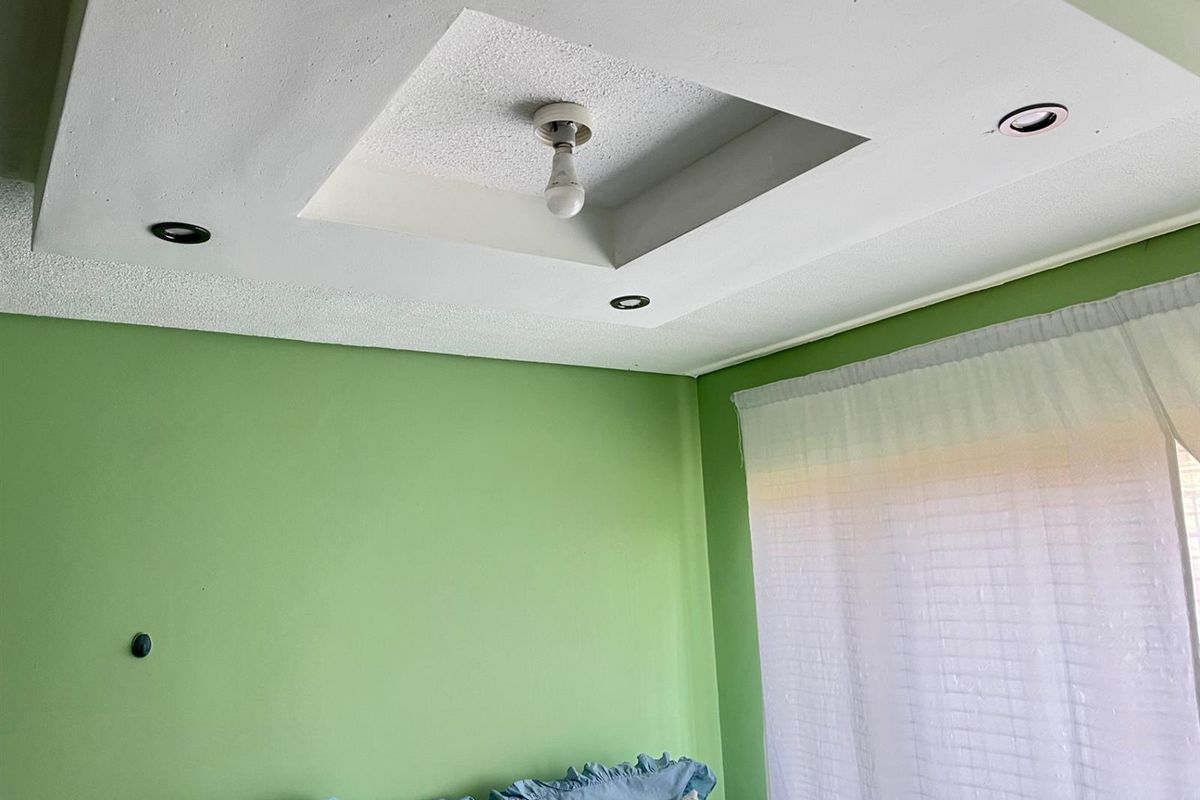 A bedroom interior featuring a recessed ceiling detail with integrated downlights and a central light fixture, finished with green painted walls.