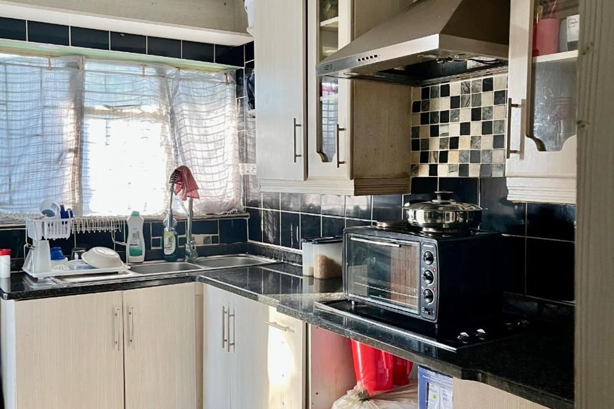 A functional kitchen featuring dark tiled splashbacks, light-toned cabinetry, a stainless steel extractor fan, and a double sink with a window view.