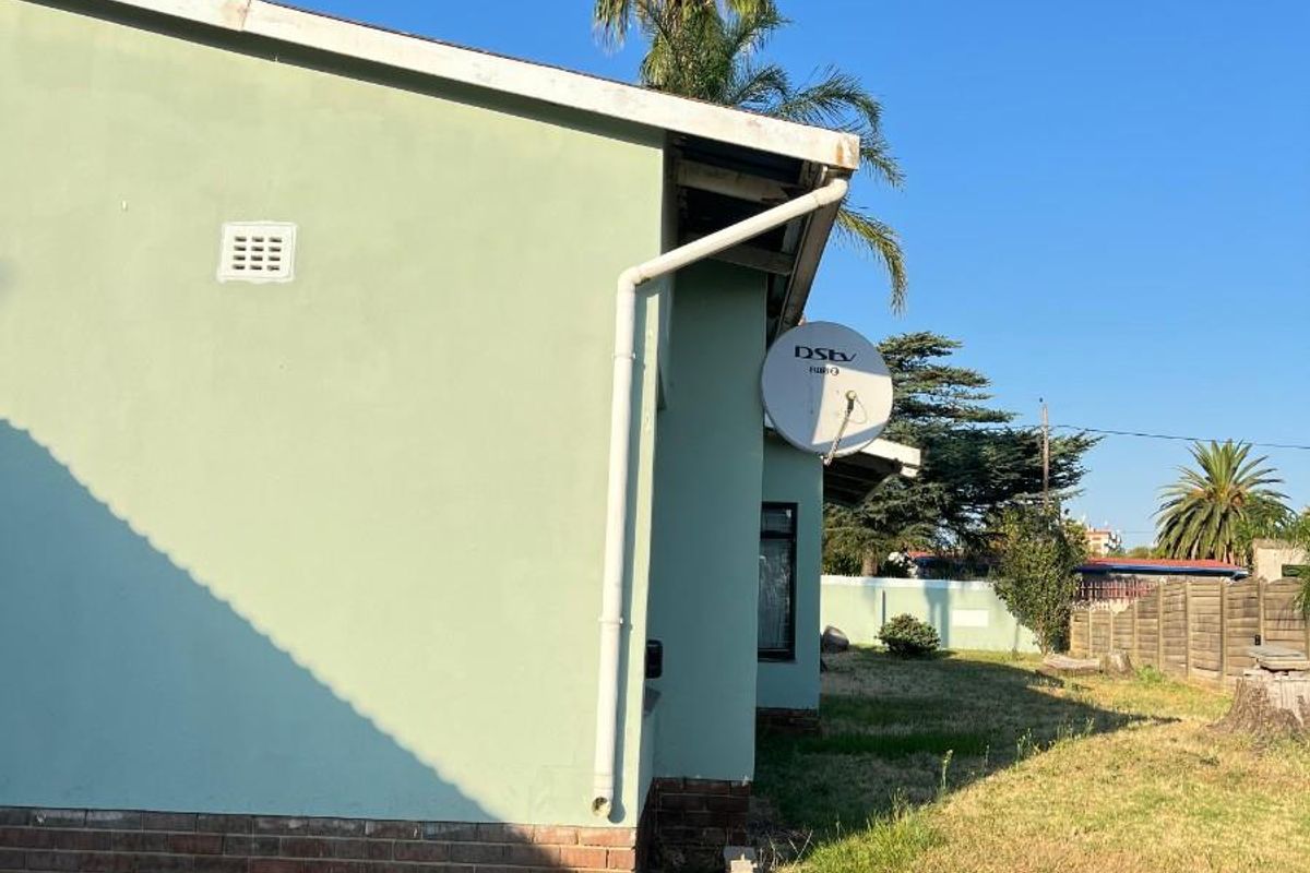 Side view of the property showing exterior wall, guttering, satellite dish, and surrounding garden area.