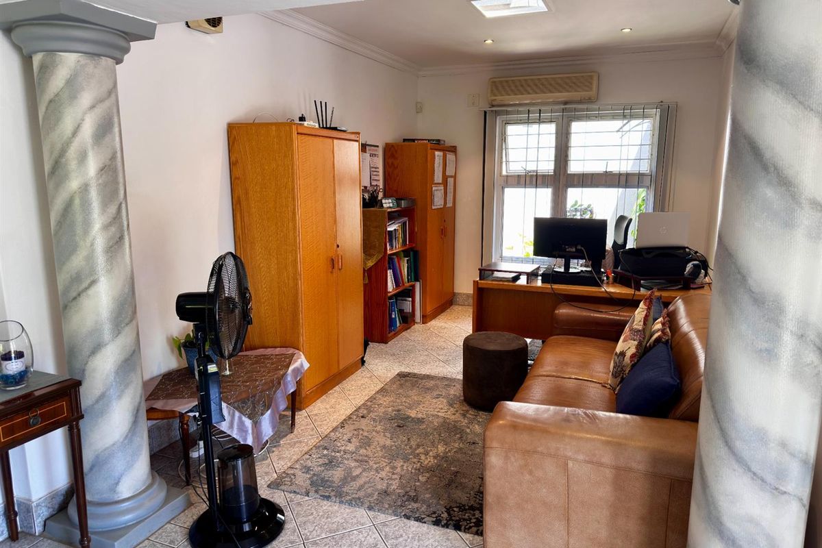 A multi-purpose living area featuring decorative columns, tiled flooring, a wall-mounted air conditioning unit, and a skylight.