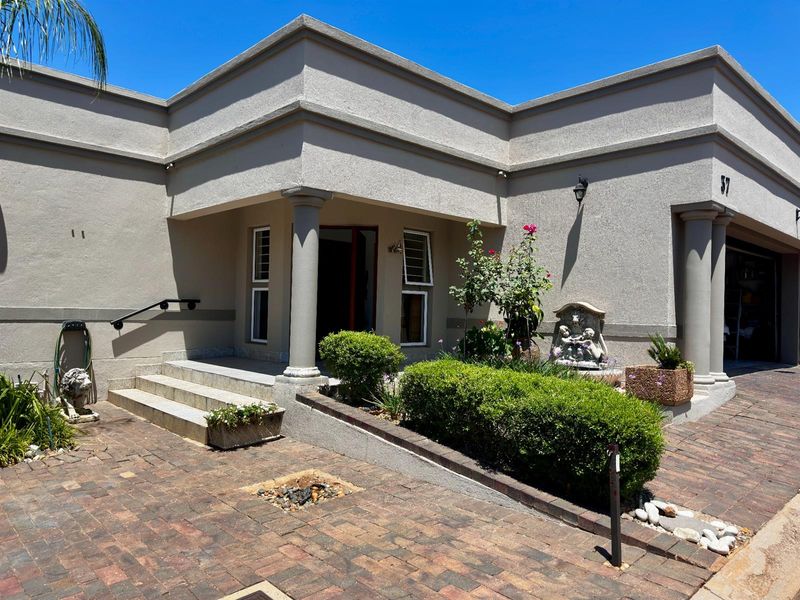 Front entrance of the house featuring a paved driveway, covered porch with columns, and landscaped garden beds.