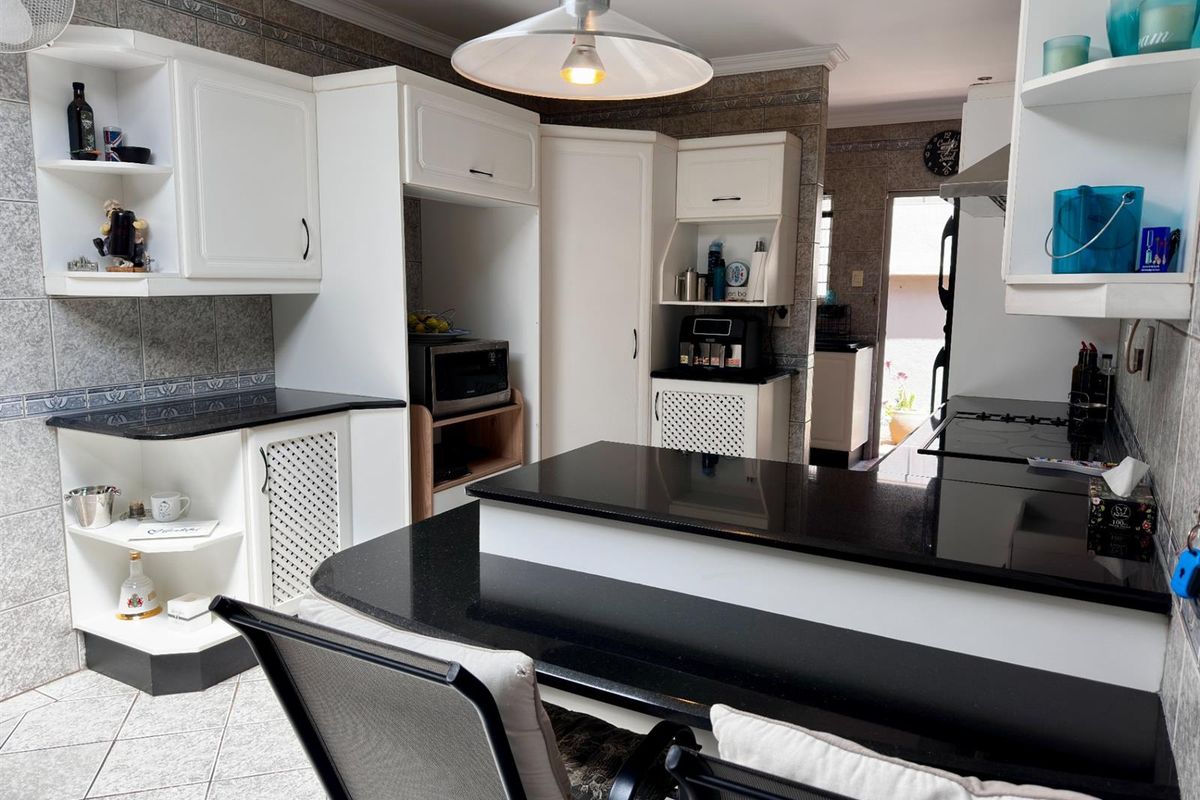 A functional kitchen featuring black granite countertops, white cabinetry, tiled walls, and a breakfast bar area with direct access to an adjacent utility space.