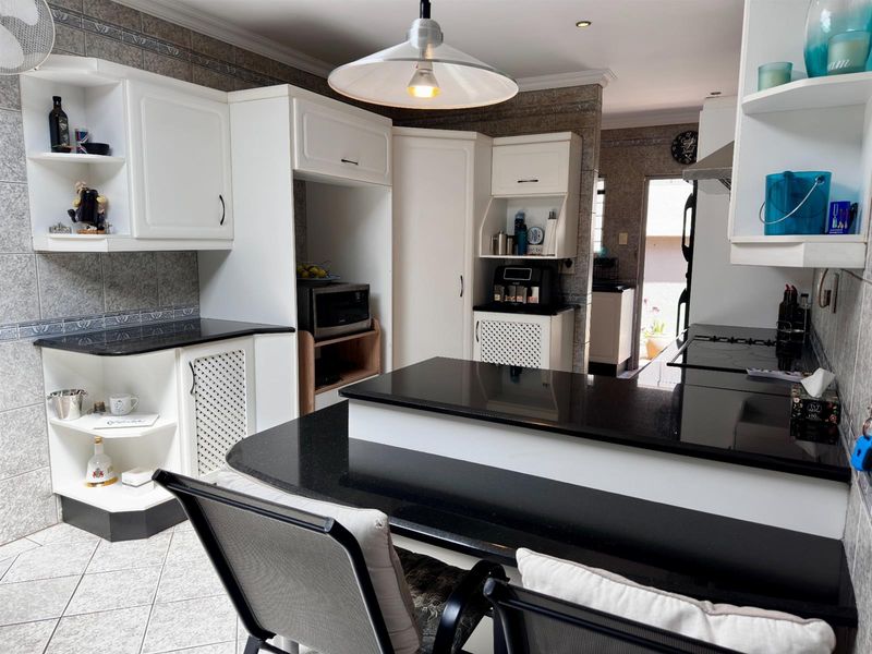 A functional kitchen featuring black granite countertops, white cabinetry, tiled walls, and a breakfast bar area with direct access to an adjacent utility space.