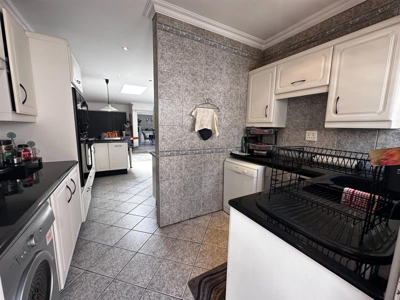 A functional kitchen featuring white cabinetry, dark countertops, and tiled finishes, with an open-plan layout leading into the adjacent living area.