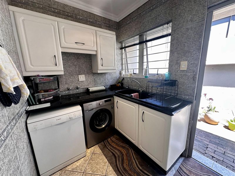 A functional laundry area featuring built-in cabinetry, a dark stone countertop, a double sink, and space for under-counter appliances with direct outdoor access.