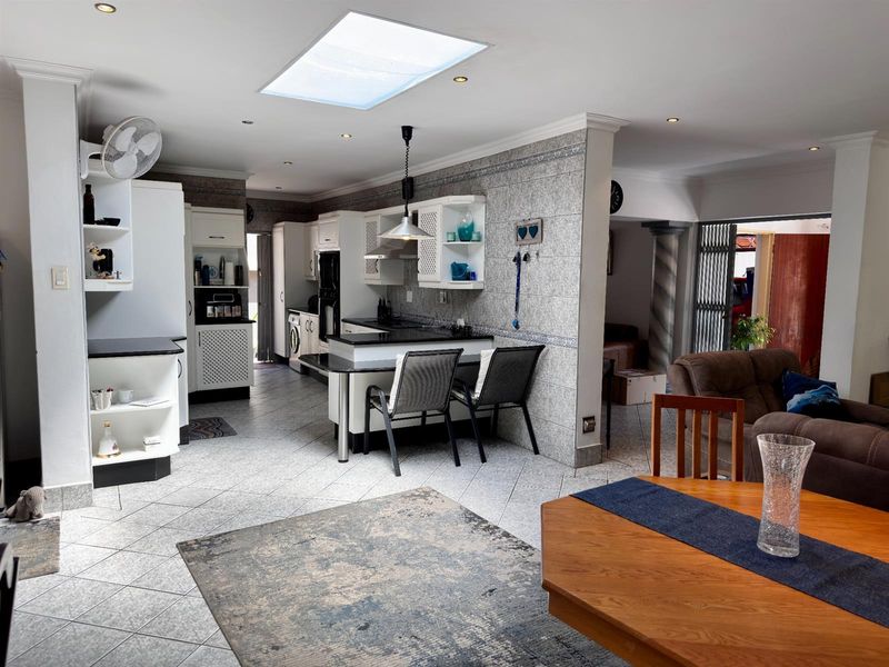 Open plan kitchen and living area featuring tiled flooring, a central breakfast bar, built-in cabinetry, and a skylight providing natural illumination.