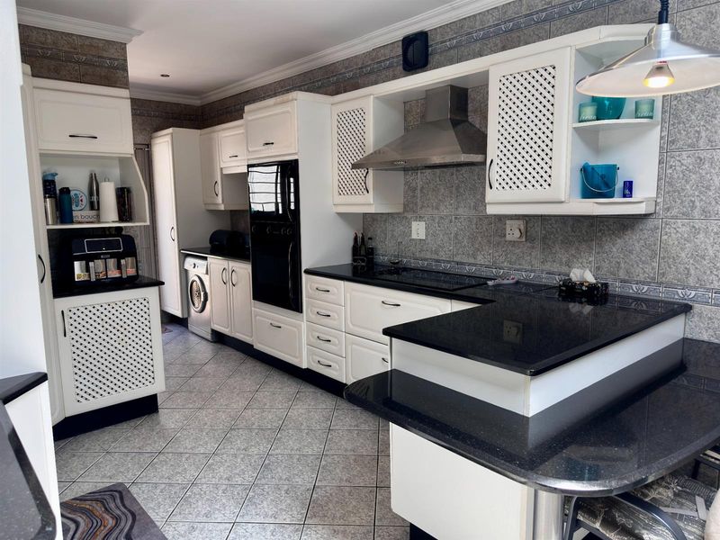 A functional kitchen featuring white cabinetry, black granite countertops, a built-in oven, stainless steel extractor fan, and tiled flooring.