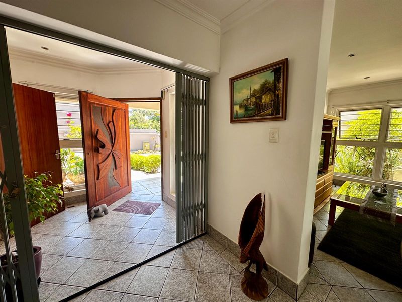 Entrance foyer featuring tiled flooring, a decorative solid wood front door, and a retractable security gate, leading into an adjacent living area.