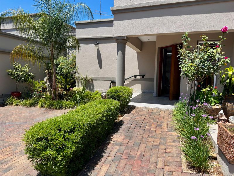A well-maintained front entrance featuring a paved walkway, landscaped garden beds, and a covered porch area with a structural column.