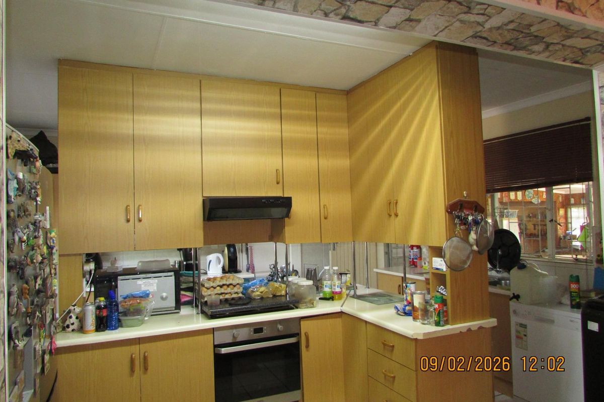 A functional kitchen featuring light wood-grain cabinetry, built-in oven, extractor fan, and a mirrored splashback, offering a practical layout for daily meal preparation.