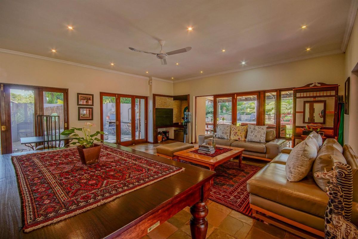 Spacious living room featuring terracotta tile flooring, recessed downlighting, a ceiling fan, and multiple wooden-framed glass doors providing access to the outdoor patio area.