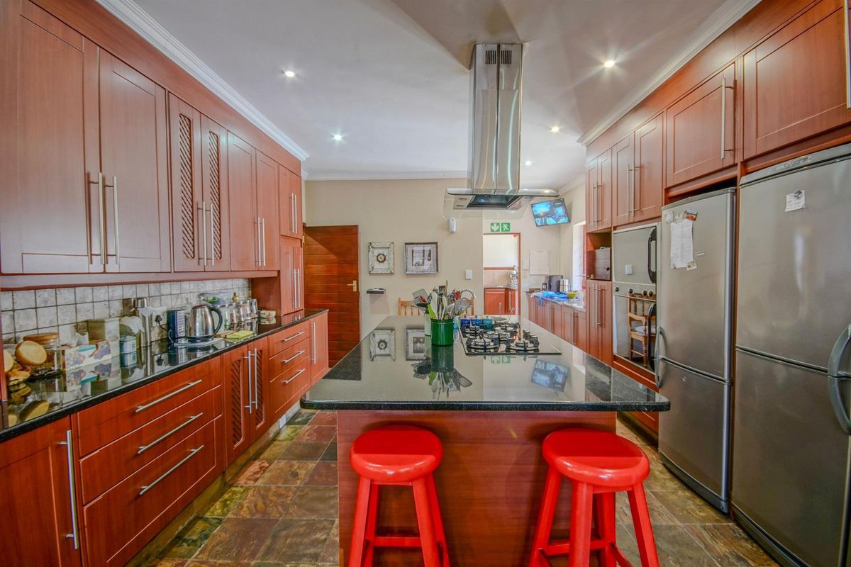 Spacious kitchen featuring dark wood cabinetry, granite countertops, a central island with a built-in gas hob, and a stainless steel extractor fan.