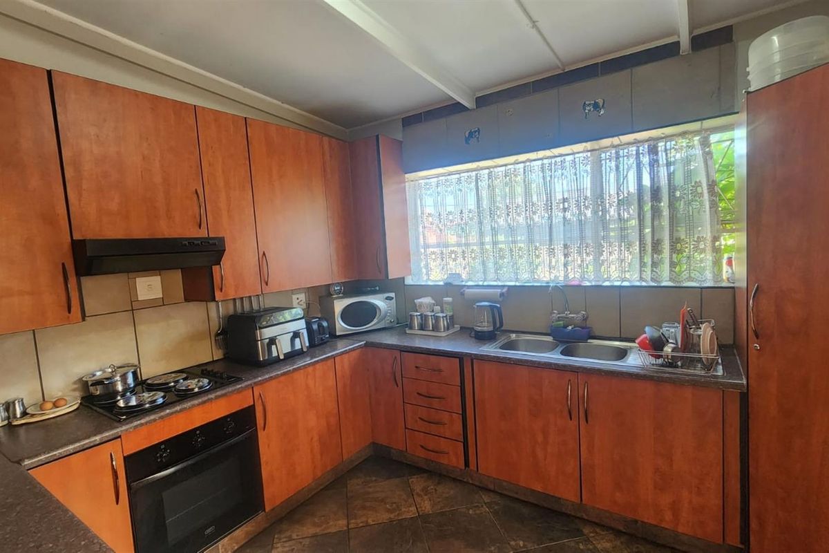 A functional kitchen featuring wood-look cabinetry, a built-in oven, hob, extractor fan, and a double-basin sink with a large window.