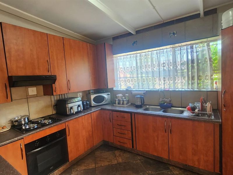 A functional kitchen featuring wood-look cabinetry, a built-in oven, hob, extractor fan, and a double-basin sink with a large window.