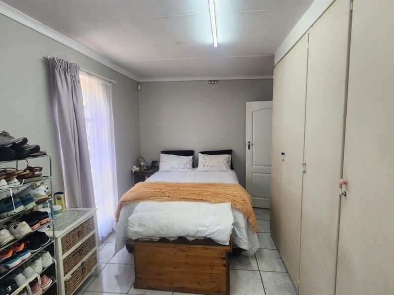 A functional bedroom featuring tiled flooring, built-in wardrobes, and a window with curtain treatments, providing a practical and comfortable living space.