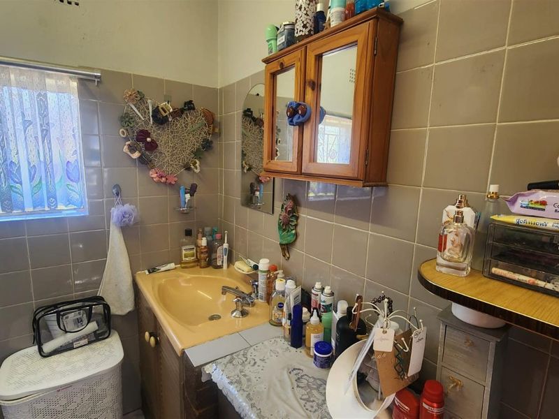 A compact bathroom featuring dated wall tiles, a built-in vanity with a basin, and a wall-mounted wooden medicine cabinet.
