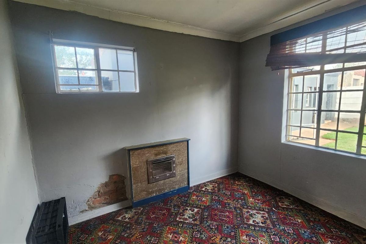 A bedroom featuring a built-in fireplace, large windows with security bars, and patterned carpeting in need of renovation.