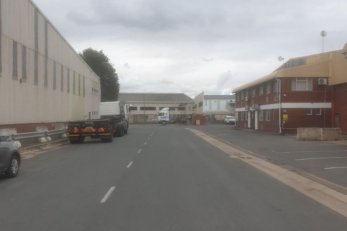 View of an industrial complex access road flanked by warehouse buildings and office facilities with paved parking areas.