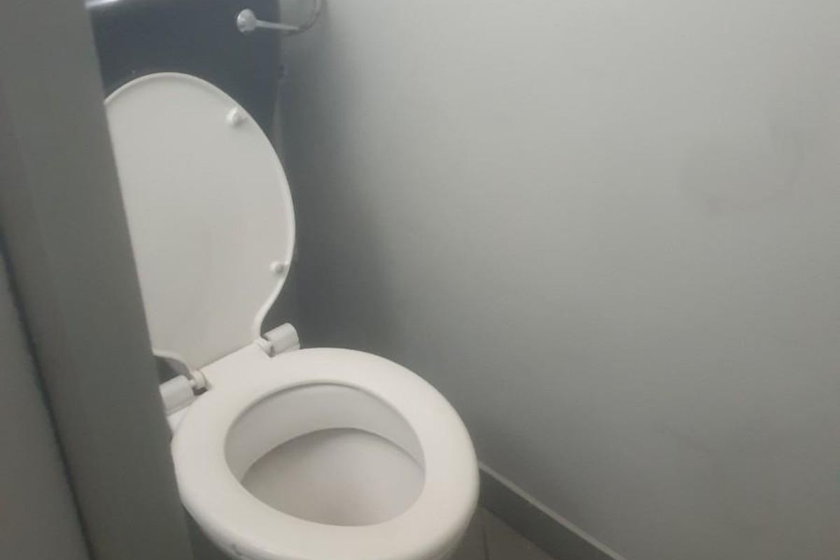 A compact industrial restroom facility featuring a standard toilet suite with a dark cistern and tiled flooring.