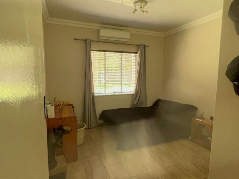 A bedroom featuring wood-look tile flooring, a wall-mounted air conditioning unit, and a window with fitted blinds.