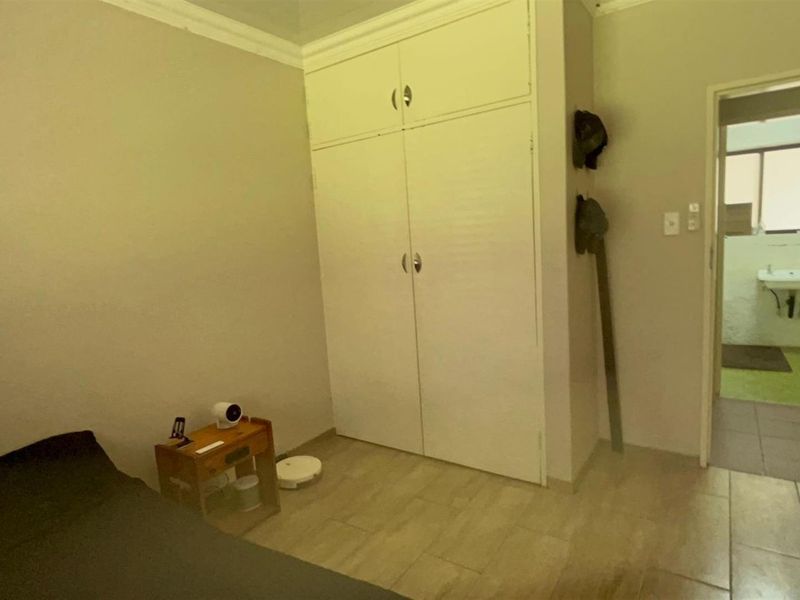 A bedroom featuring built-in cupboards and tiled flooring, with an adjacent view into a bathroom area.