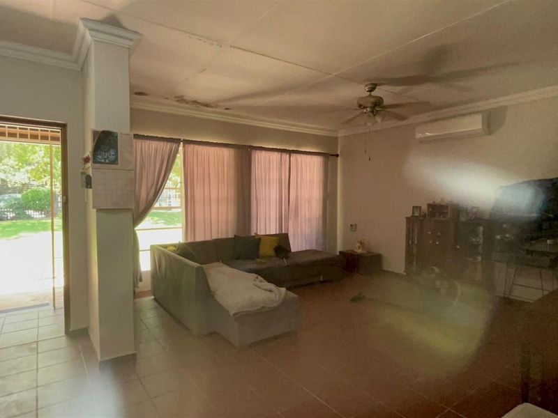 Spacious living area featuring tiled flooring, a ceiling fan, and wall-mounted air conditioning unit, with direct access to the garden.