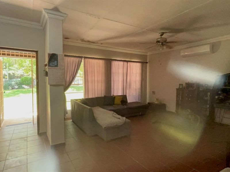 Spacious living area featuring tiled flooring, a ceiling fan, and wall-mounted air conditioning unit, with direct access to the garden.
