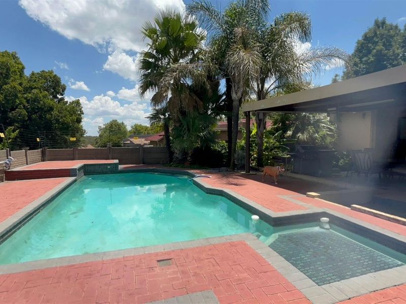 Outdoor pool area featuring a swimming pool with integrated spa, paved surround, and a covered patio area.