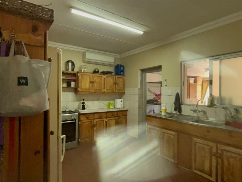 A dated kitchen featuring wooden cabinetry, a stainless steel sink, and a wall-mounted air conditioning unit.