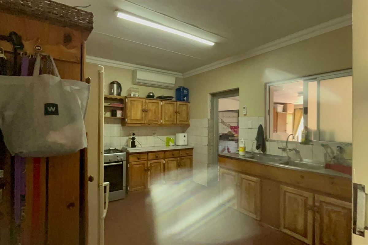 A dated kitchen featuring wooden cabinetry, a stainless steel sink, and a wall-mounted air conditioning unit.