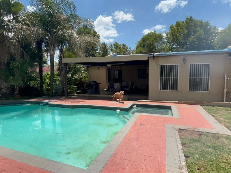 Rear exterior view featuring a swimming pool, paved surround, and a covered patio area, set within a landscaped garden.