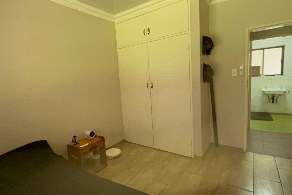 A bedroom featuring built-in cupboards and tiled flooring, with an adjacent view into a bathroom area.
