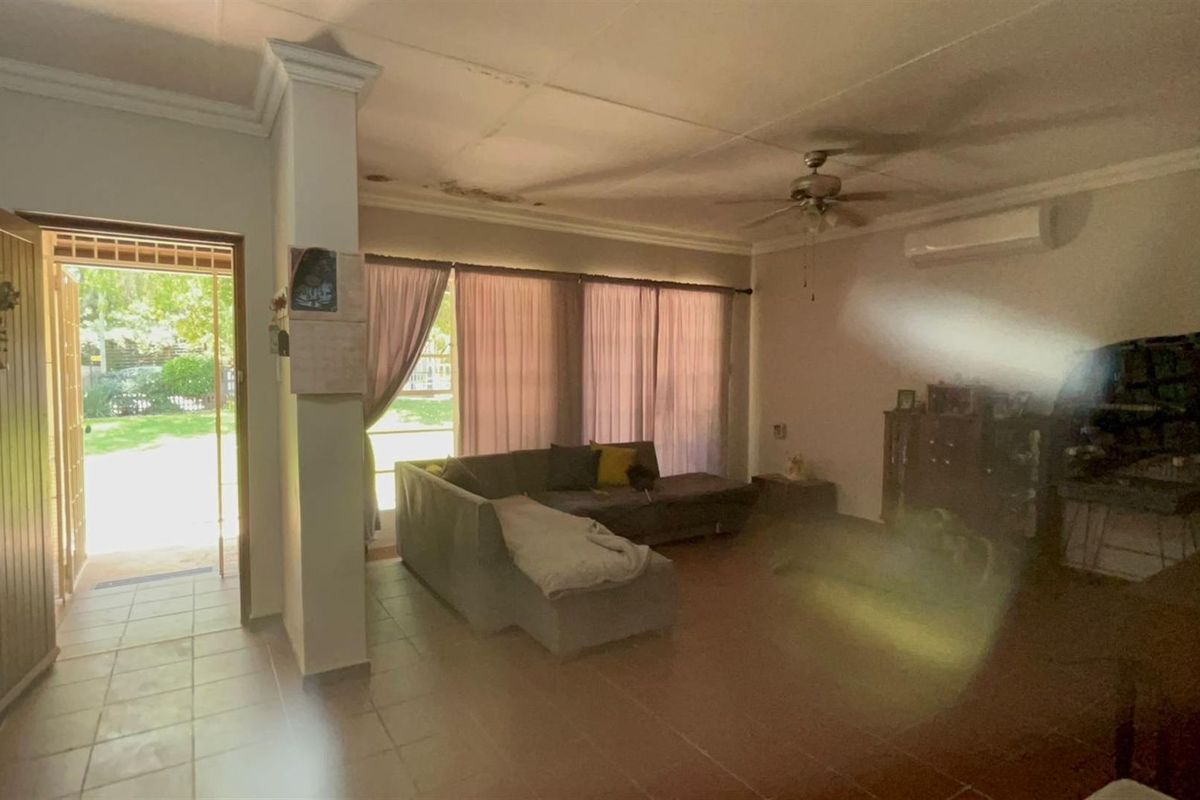 Spacious living area featuring tiled flooring, a ceiling fan, and wall-mounted air conditioning unit, with direct access to the garden.