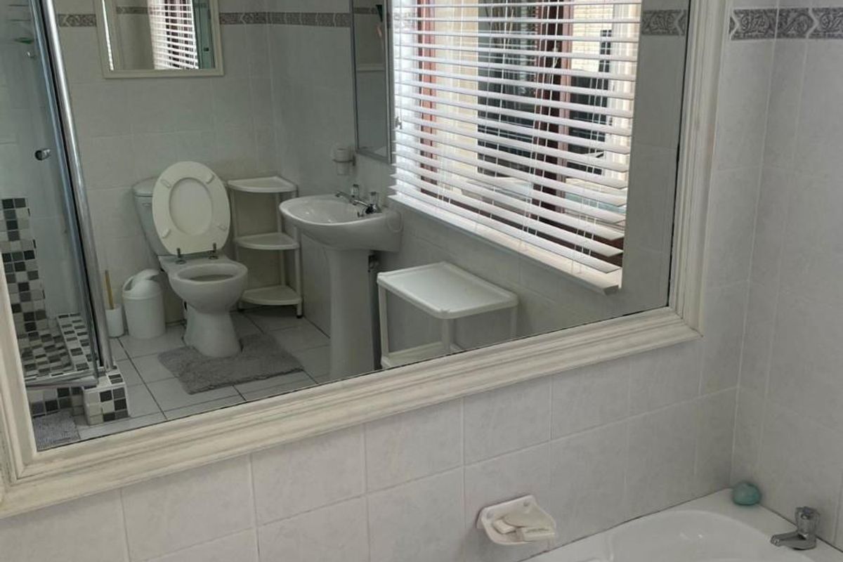 A functional bathroom featuring a white bathtub, pedestal sink, toilet, and a glass-enclosed shower, finished with wall tiling and a large vanity mirror.