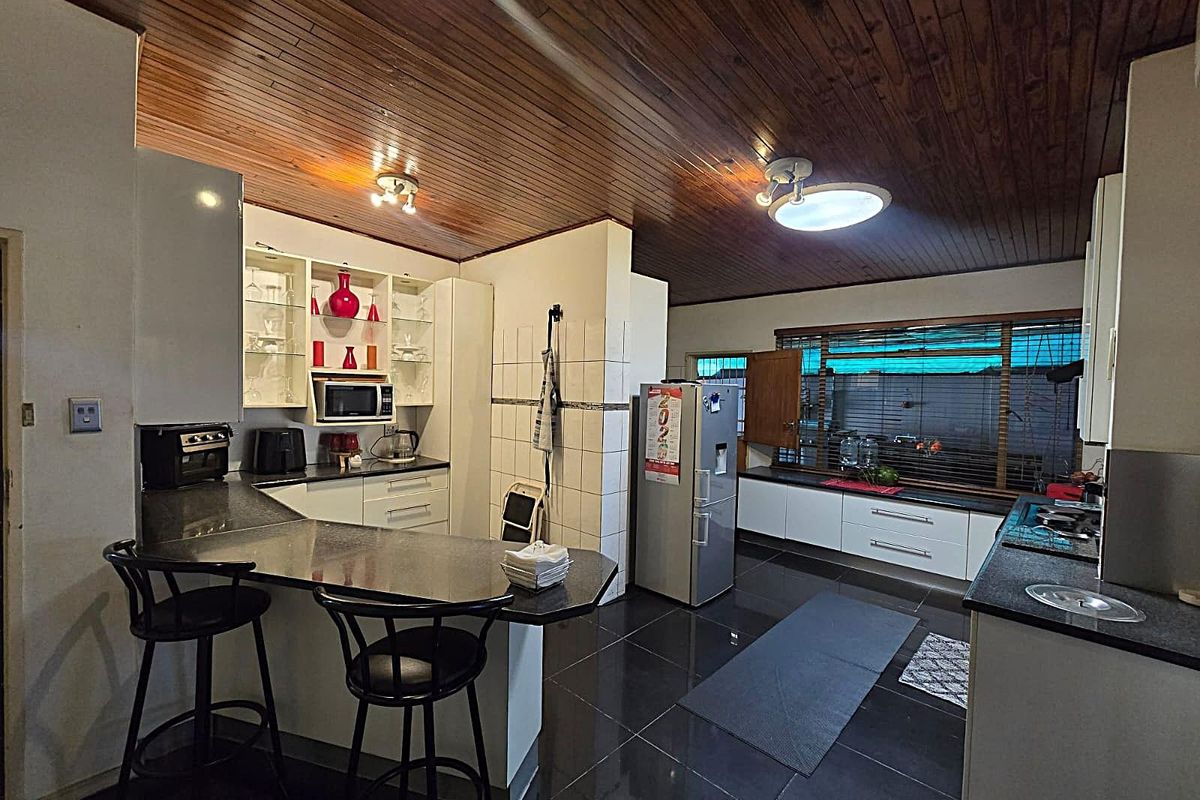Spacious kitchen featuring dark granite countertops, white cabinetry, a breakfast bar, and a distinctive timber-paneled ceiling with integrated lighting.