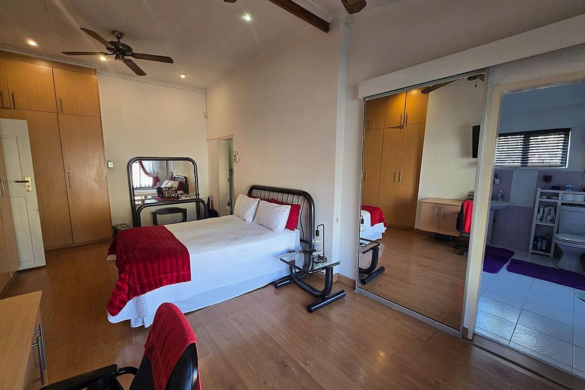 Spacious bedroom featuring built-in wooden cupboards, laminate flooring, a ceiling fan, and an en-suite bathroom with mirrored sliding doors.