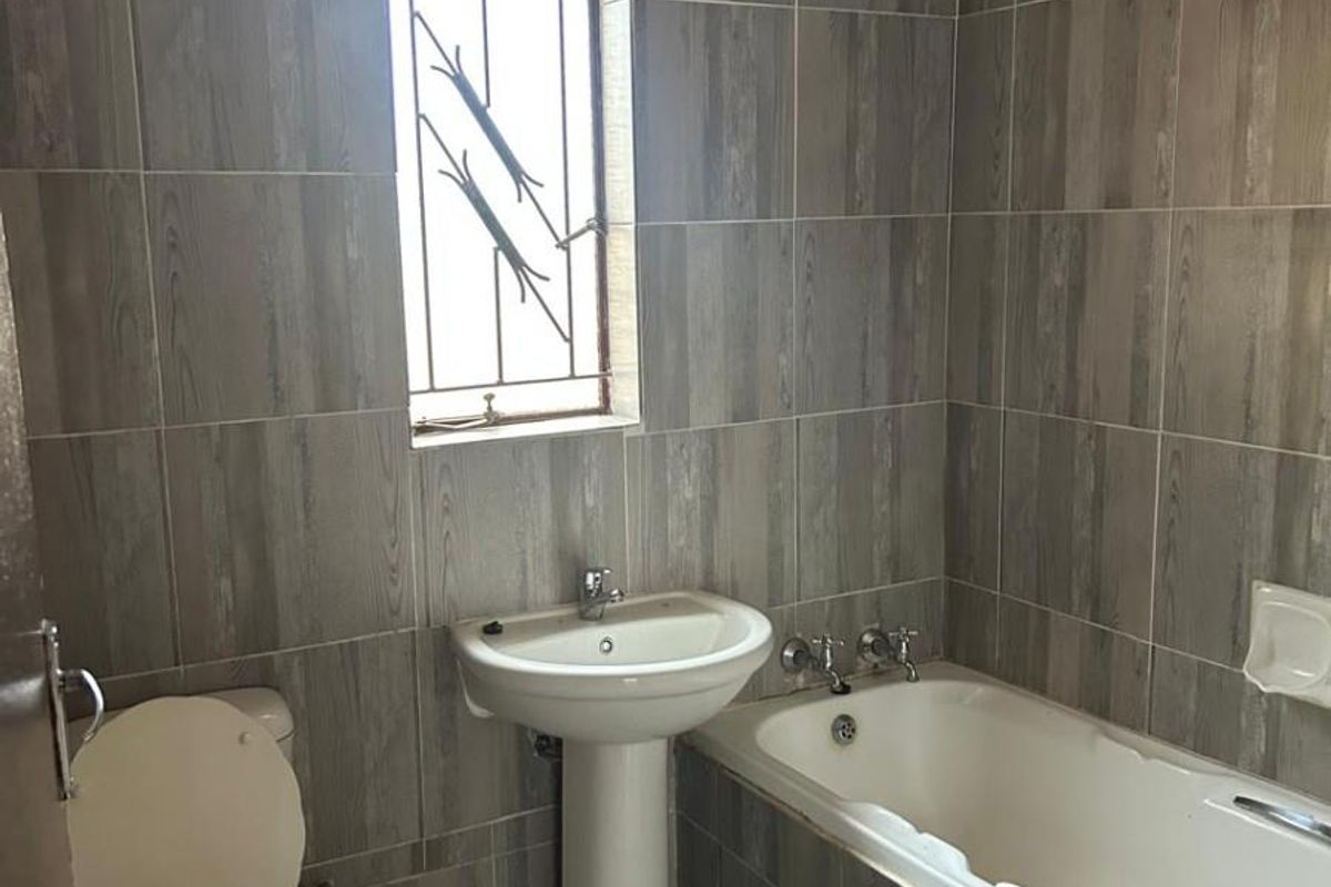 A functional bathroom featuring wood-look wall tiles, a pedestal basin, a standard bathtub, and a security-barred window.