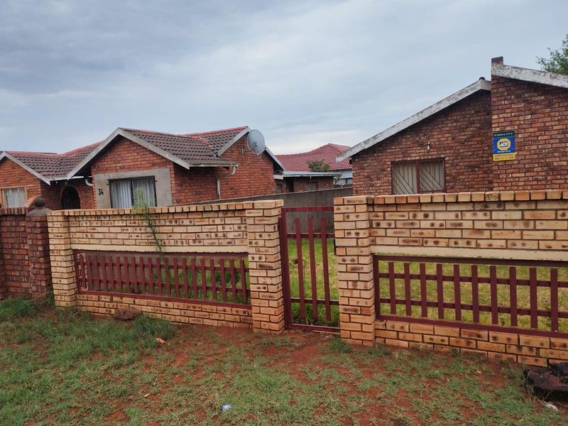 A view of the front exterior of a brick house featuring a perimeter brick wall with a metal gate and tiled roof.