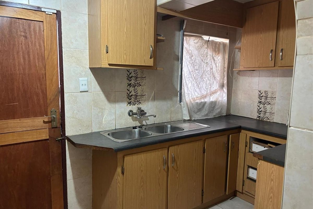 A dated kitchen featuring wood-look cabinetry, laminate countertops, a double-basin stainless steel sink, and tiled wall splashbacks.