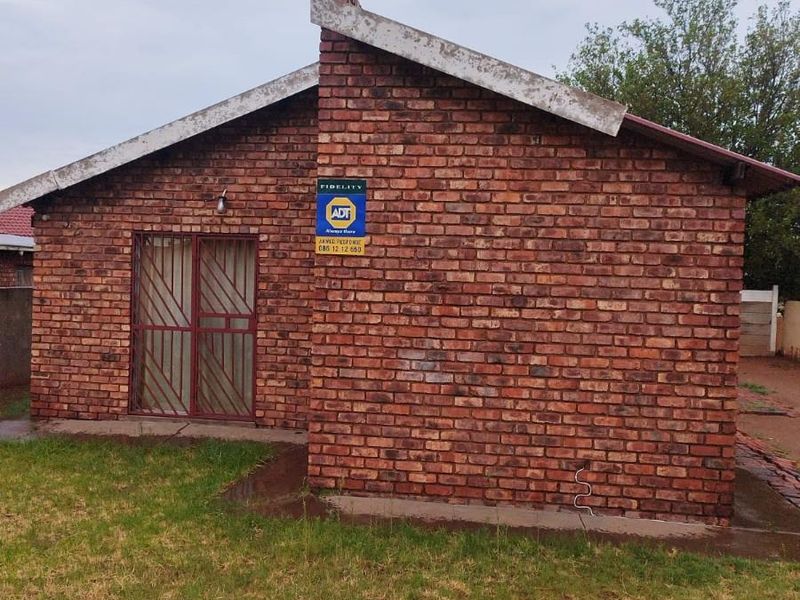 A side view of a face-brick residential building featuring a security gate and an installed alarm system.