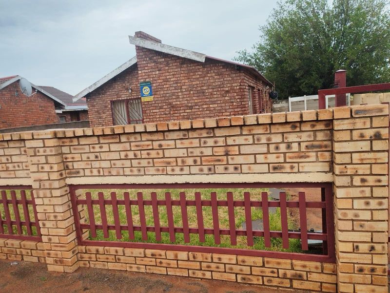 A view of the property exterior featuring a face-brick facade and a secure perimeter wall with integrated metal fencing.