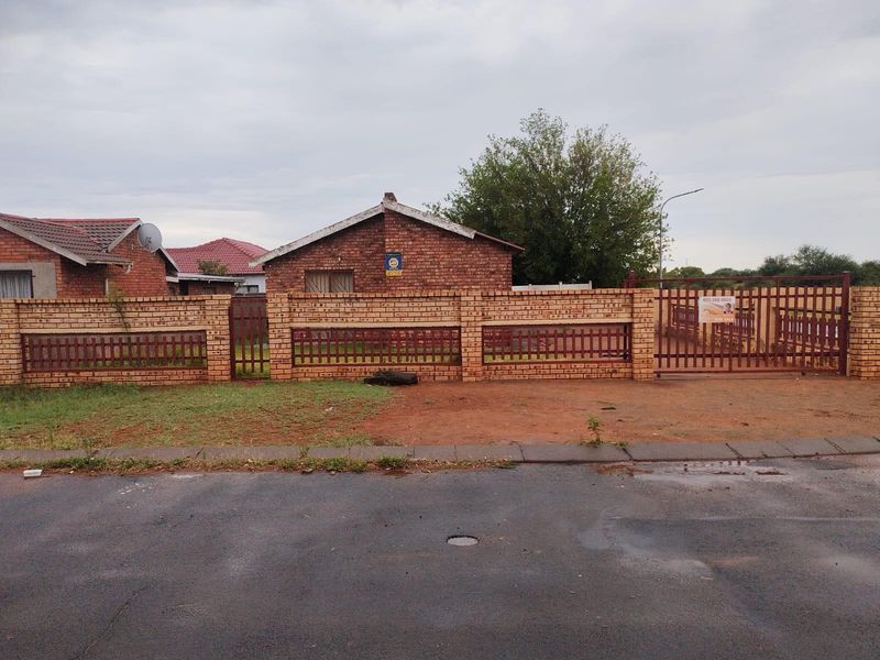 A street-facing view of a single-story brick house featuring a perimeter brick wall with integrated metal fencing and a gated driveway entrance.
