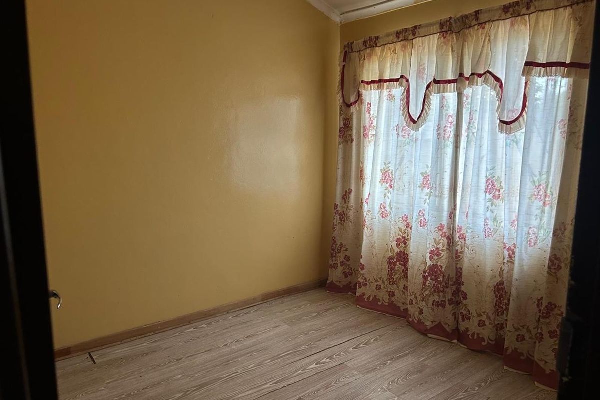 A bedroom featuring wood-look laminate flooring and yellow painted walls, with a large window covered by floral curtains.