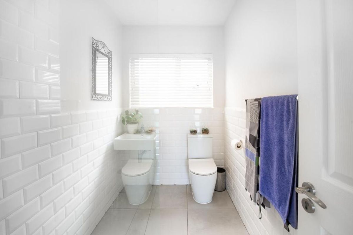 A clean, modern bathroom featuring white subway tile wall cladding, a wall-mounted basin, a toilet, and neutral floor tiles.