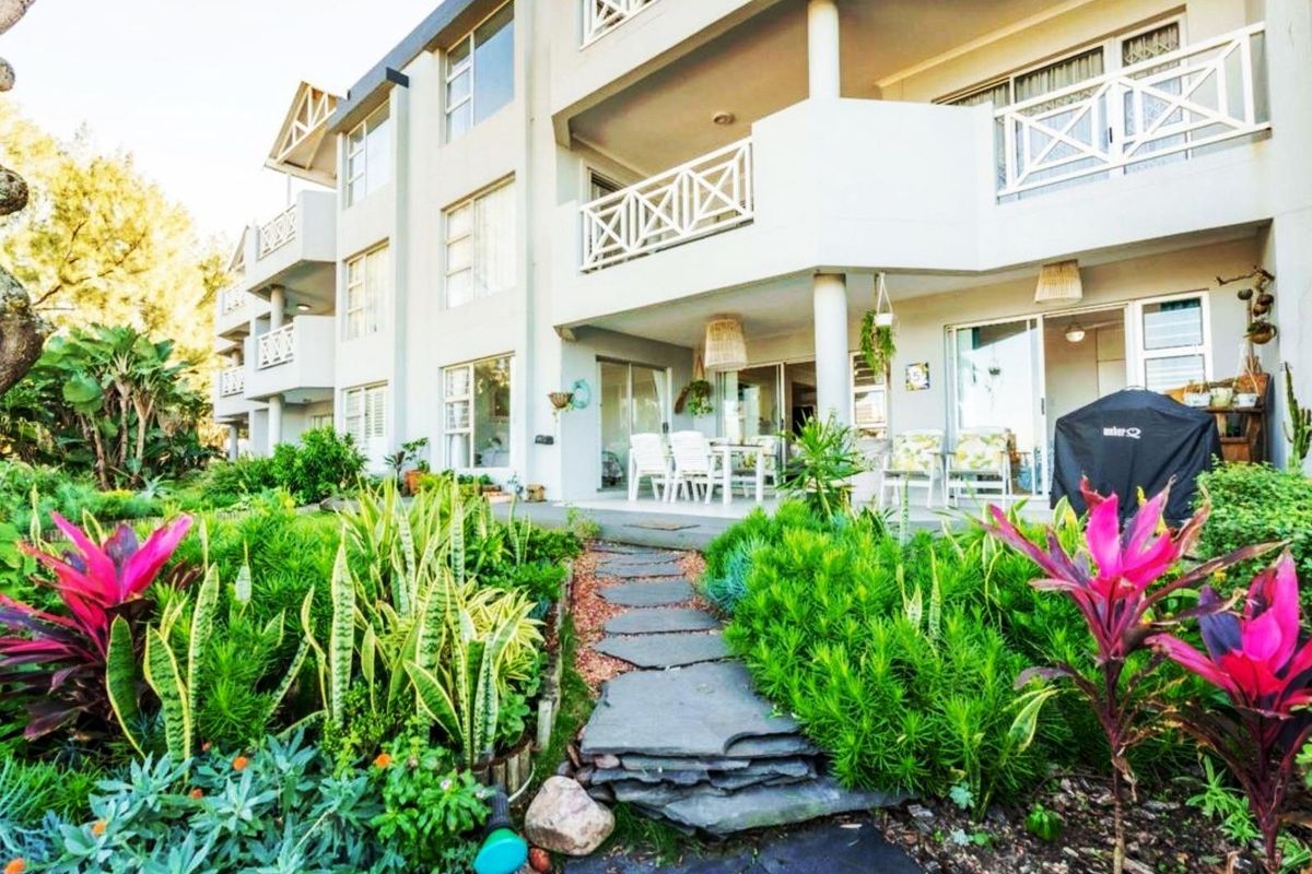 Rear view of the apartment building featuring a landscaped garden, stone pathway, and private balconies with sliding glass door access.