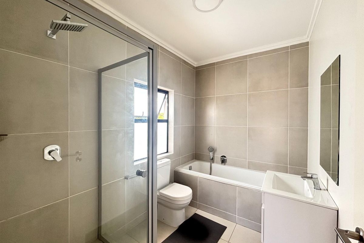 Modern bathroom featuring a glass-enclosed shower, a built-in bathtub, a vanity basin, and neutral floor-to-ceiling tiling.