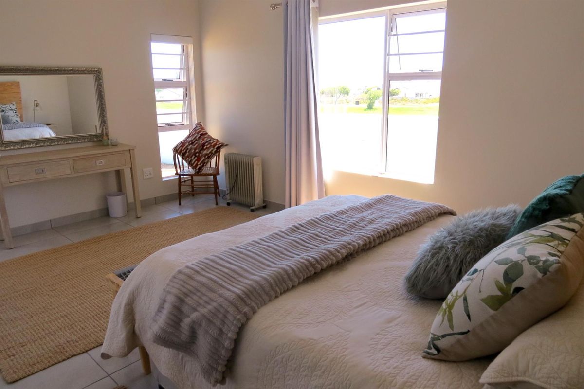 A bright and airy bedroom featuring neutral tiled flooring, large windows with aluminium frames, and a clean, minimalist aesthetic.