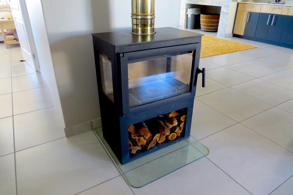 A modern freestanding wood-burning fireplace with a glass hearth plate, situated in an open-plan living area with tiled flooring.