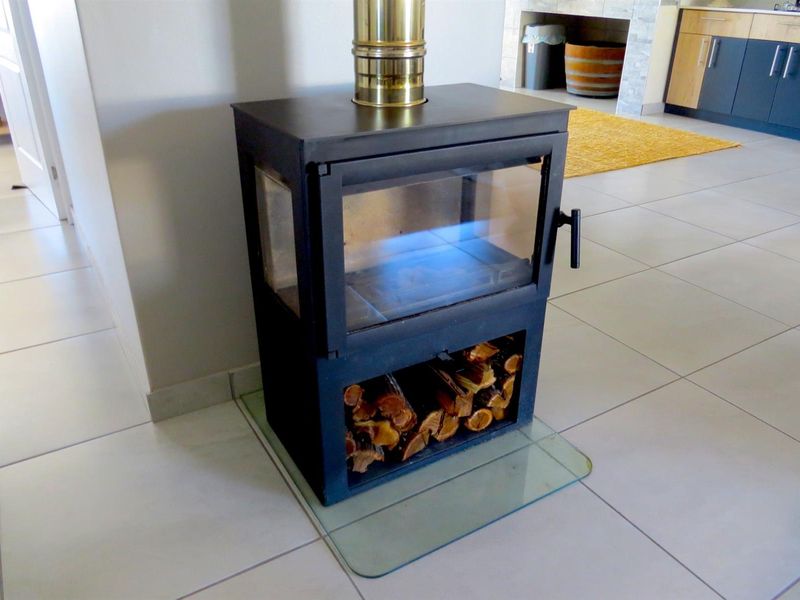A modern freestanding wood-burning fireplace with a glass hearth plate, situated in an open-plan living area with tiled flooring.