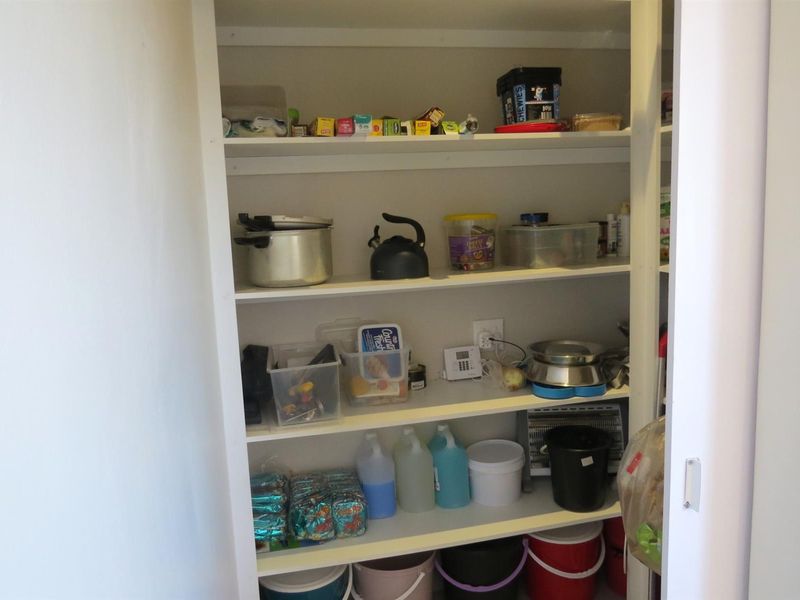 A functional walk-in pantry or scullery storage area featuring multiple built-in shelves for organized storage and an integrated electrical outlet.